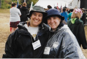 My Mom and I smiling and standing side by side with arms around each other's backs. I'm in a black and blue rain jacket with a green bucket hat, my a blue bucket hat and clear plastic raincoat. In the background are women milling about
